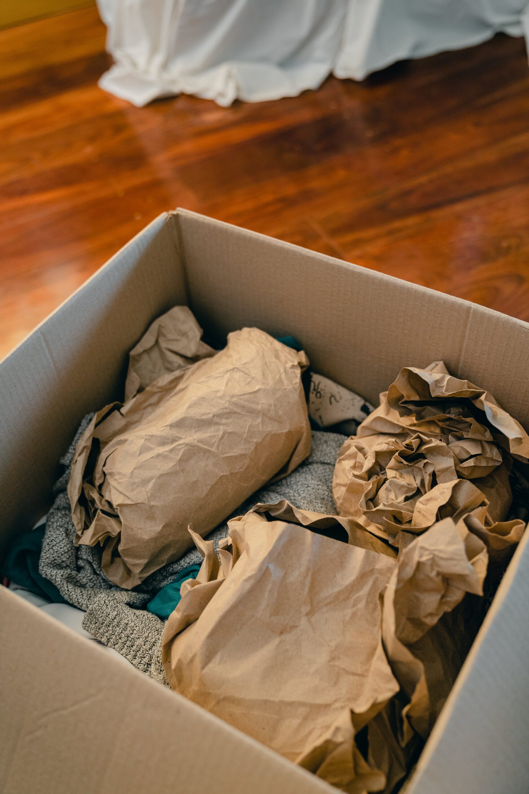 From above of open cardboard box full of fragile items wrapped in packaging paper for protection.