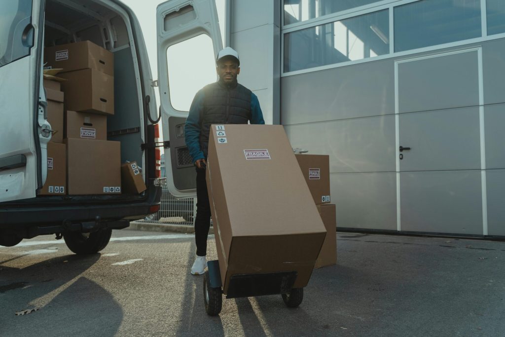 Delivery person pushing a cart with a large cardboard box that was pulled out of a delivery van.